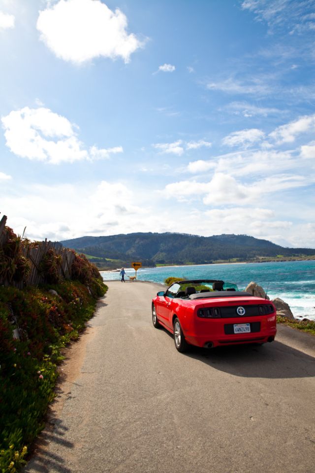 Driving along California's Pacific Coast Highway in a hot red convertible car.