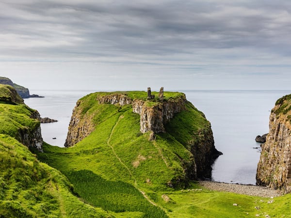 Beautiful fresh green northern ireland coastal landscape towards the atlantic ocean with the gate lodge ruins on small peninsula at Dunseverick