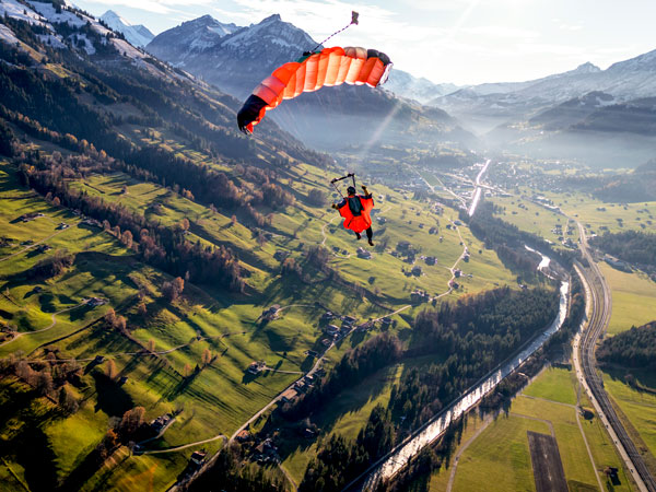 Paraglider flies through clear skies in the morning with the Sunny Swiss Alps below.