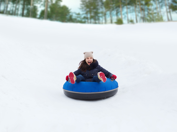 winter, leisure, sport, and people concept - happy teenage girl or woman sliding down on snow tube