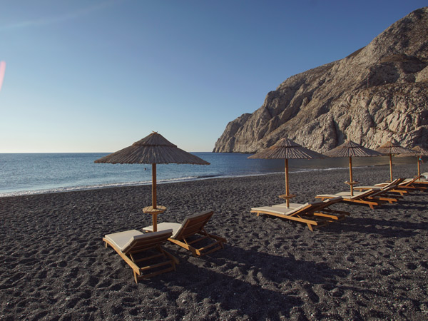 Day beds on black sand Kamari Beach, Santorini.
