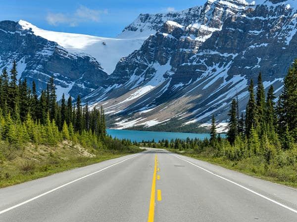 A Spring evening view of Icefields Parkway extending towards Bow Lake, with BowCrow Peak, Crowfoot Glacier and Crowfoot Mountain rising high behind, Banff National Park, Alberta, Canada