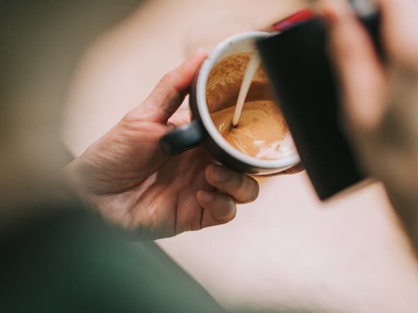 A barista pouring froth milk on coffee cup prepared coffee latte art at bar counter.