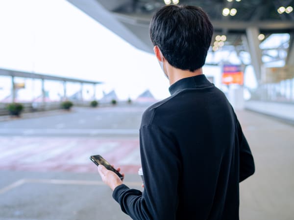 Asian man wearing a face mask and checking uber / taxi / grab in Bangkok, Thailand.