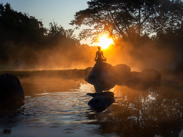 A person meditates at sunrise next to a hot spring.