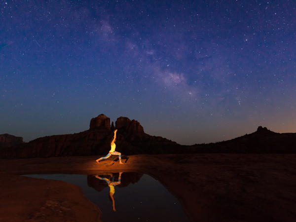 a woman reflected practicing yoga under the milky way near cathedral rock sedona arizona