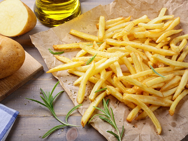 French fries on brown paper with olive oil, rosemary and a potato