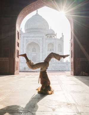 Young woman practicing yoga in India at the famous Taj Mahal at sunrise - Headstand position upside down- People travel spirituality zen like concept