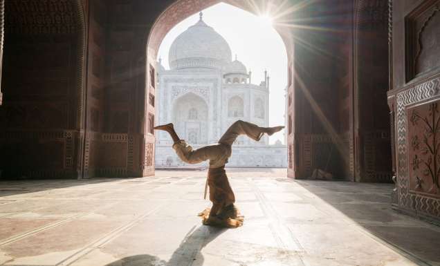 Young woman practicing yoga in India at the famous Taj Mahal at sunrise - Headstand position upside down- People travel spirituality zen like concept