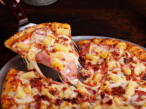 Slice of Hawaiian pizza being lifted.