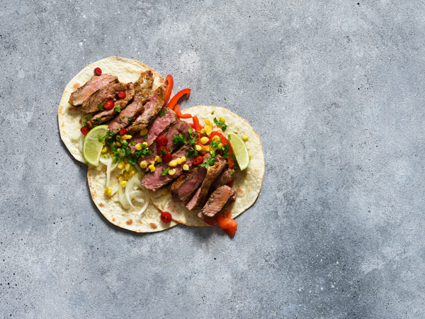 Fajitas with beef, pepper and corn with sauce on a concrete background.