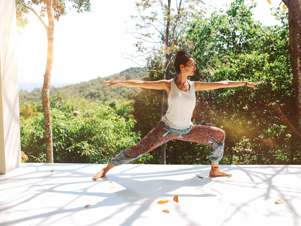 Young woman doing morning yoga exercise at her home terrace in Koh Phangan island in Thailand. She is doing stretching and meditation, relaxing on the beginning of a new day.