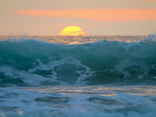 A wave crashing in the foreground of a sunset