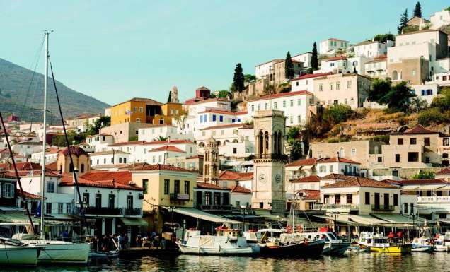 Wide shot of boats on Hydra Harbour with buildings around. Greece.