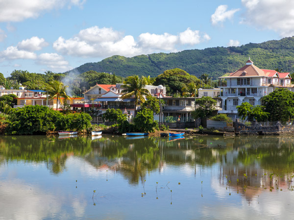 A photo of a village on a lake with mountains in the back.