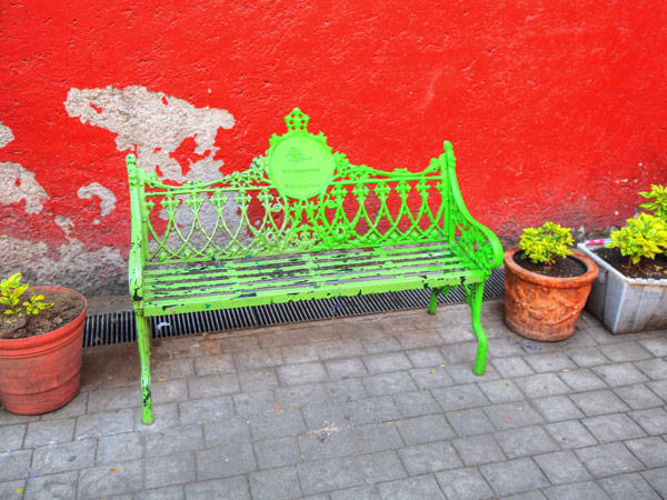a green bench beside potted plants on red wall background