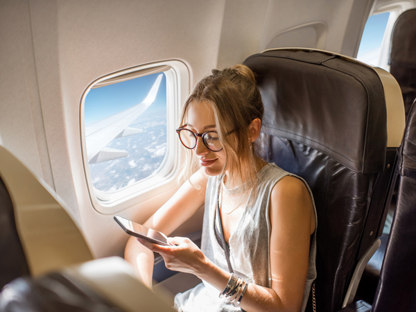 Young woman sitting with phone on the aircraft seat near the window during the flight in the airplane