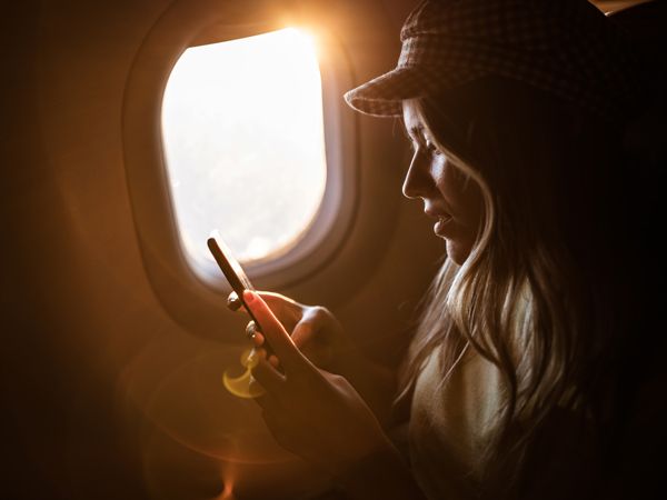 Young woman using mobile phone while traveling by airplane at sunset