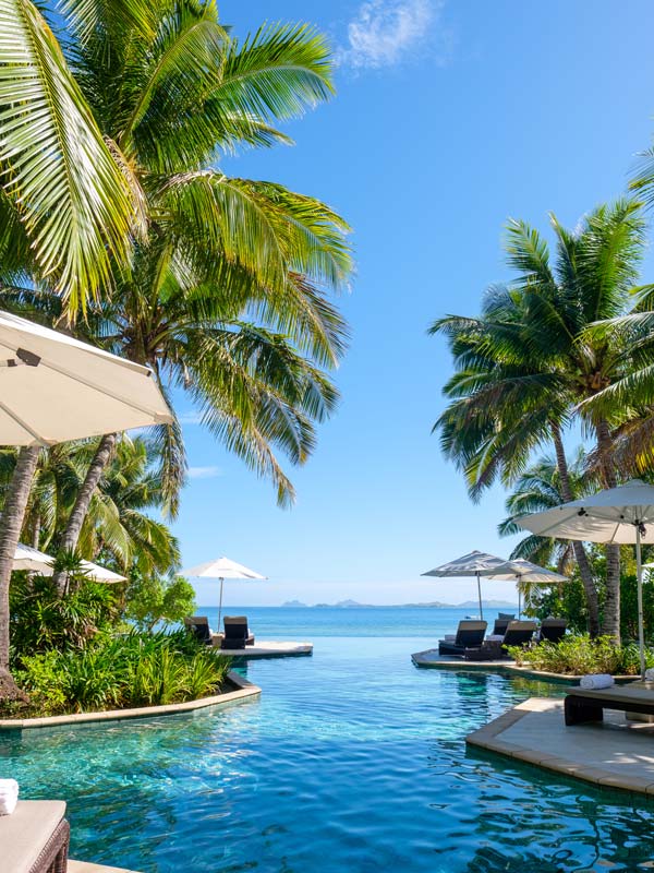 an outdoor pool with palm trees in the background at Likuliku