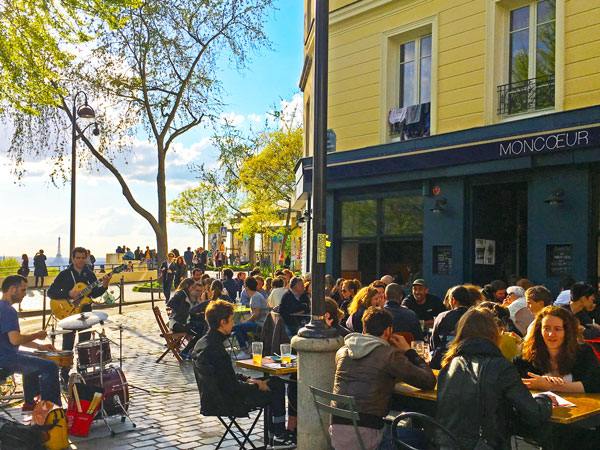 customers sitting outside Moncoeur Belleville with Parisian street performers on the side