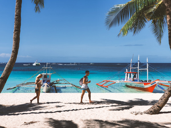 tourists walking by the beach with boats parked on Boracay Island
