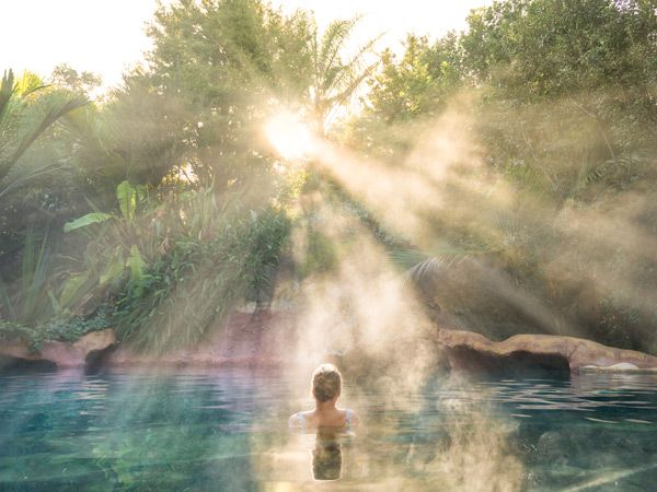 bright rays of sunshine directly pointing towards a woman soaking in The Lost Spring NZ