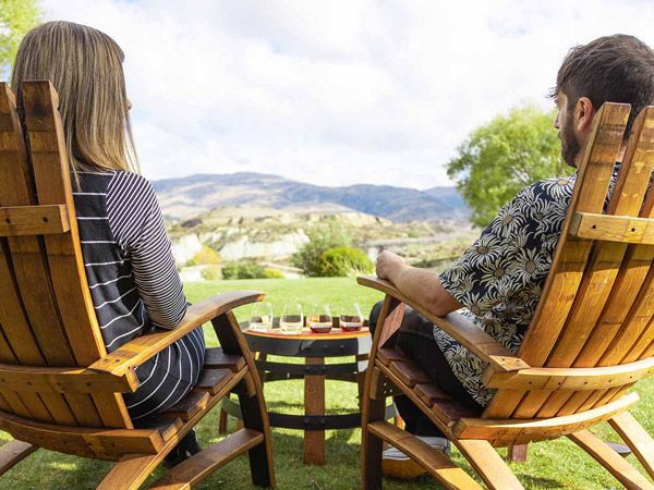 Carrick winery tasting flight at the Bannockburn Inlet in Central Otago New Zealand showing a couple enjoying wines with the vineyard and mountain backdrop of the Bannockburn sub-region