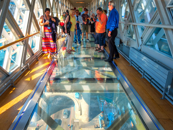 visitors standing on the edge of a glass pathway at the Tower Bridge, London