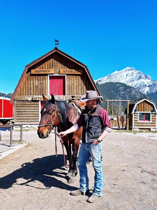 a man standing beside a horse at Banff Trail Riders