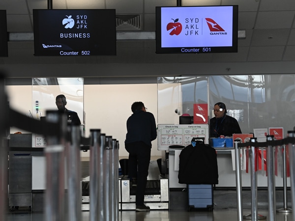 a guy standing at the check-in counter for Qantas Flight QF3 Auckland to New York