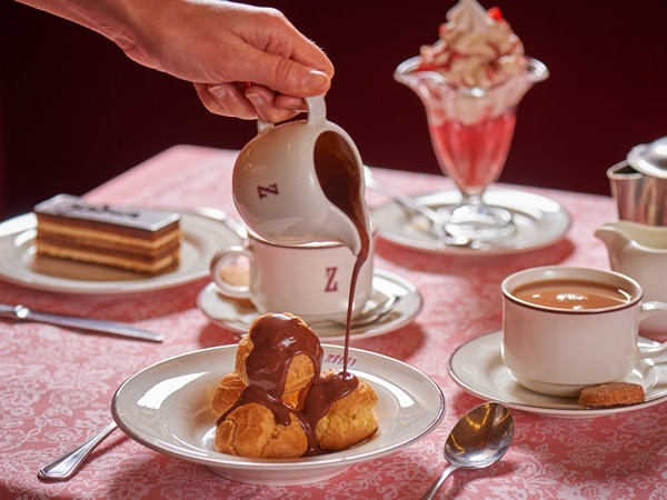 a hand pouring chocolate filling on top of Profiteroles at Brasserie Zedel