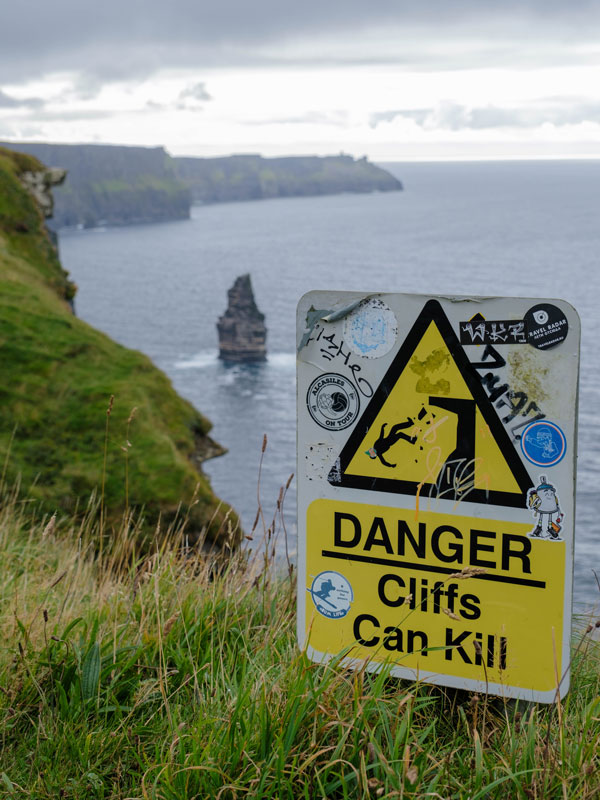 a vandalized warning sign in front of the Cliffs of Moher