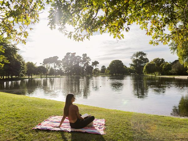 a woman relaxing and sitting on a blanket on the grass at Hagley Park, Christchurch