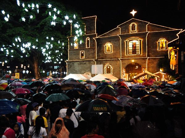 Filipinos attending Misa De Gallo while seeking shade from the rain