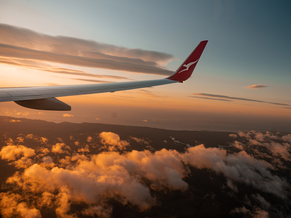 Wing of a Qantas aircraft in the clouds at sunrise