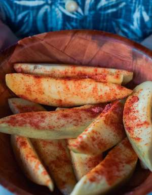 a hand holding a bowl filled with sliced mangoes sprinkled with salty plum powder