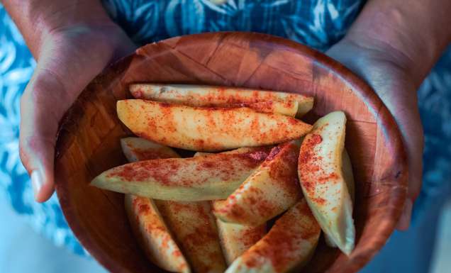 a hand holding a bowl filled with sliced mangoes sprinkled with salty plum powder