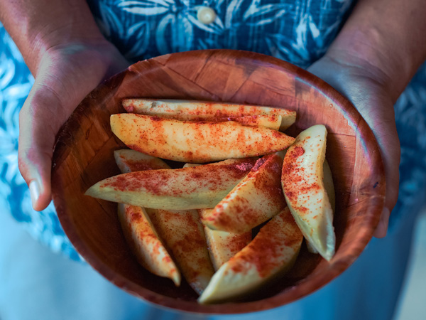 a hand holding a bowl filled with sliced mangoes sprinkled with salty plum powder