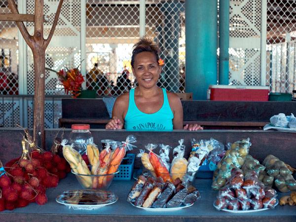 a vendor smiling to greet visitors at a Moorea market stall