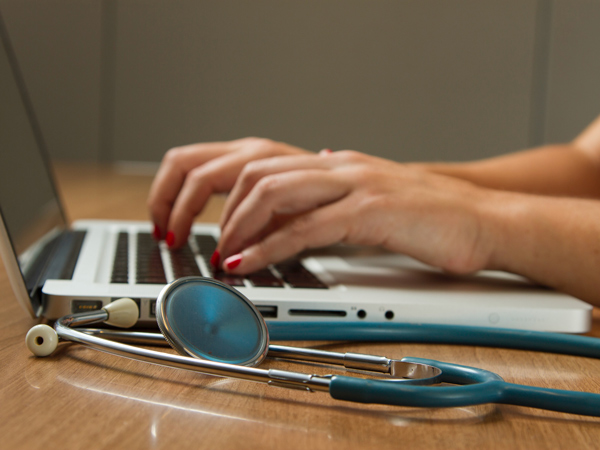 a hand typing on a laptop keyboard beside a stethoscope