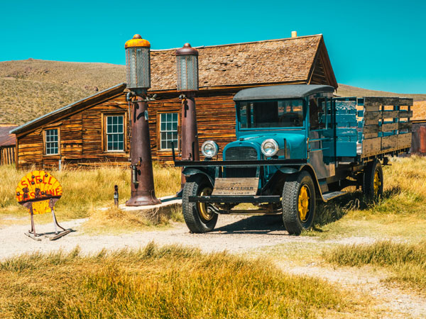 a vintage car parked beside a brown brick structure under the blue sky in Bodie, California, USA
