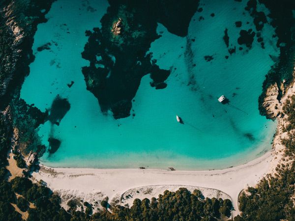a drone shot of a white sand beach and emerald blue waters at Plage de Roccapina, Corsica
