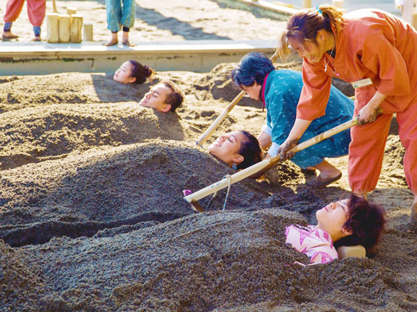 guests lying down in the sand while getting raked at Beppu sand bath