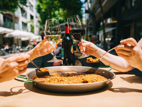 holding wine glasses with a big plate of paella on the table