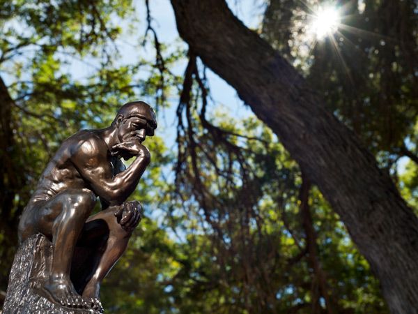 a small bronze replica of Rodin's The Thinker statue sitting under the tree