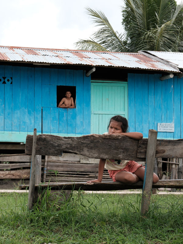 a child sitting on a wooden bench with a young boy behind him looking out from the window in Bolivar