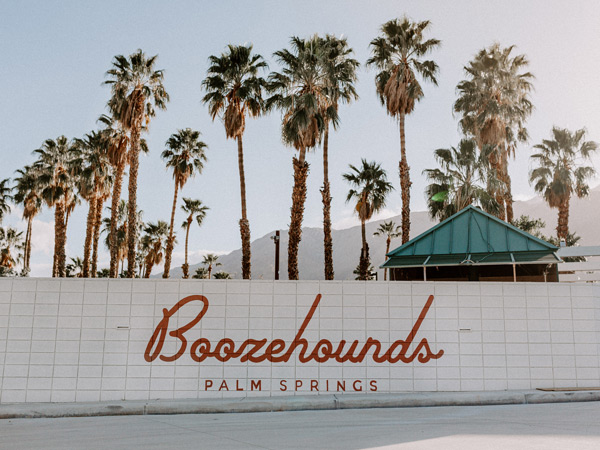 the Boozehounds Palm Springs signage against a backdrop of tall palm trees