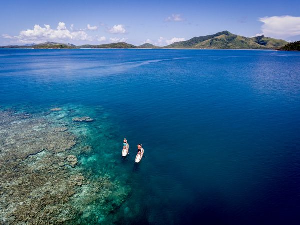 an aerial view of two people paddleboarding around Turtle Island, Fiji