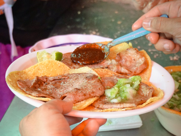 a hand pouring sauce over beef tacos at Taquería El Califa de León