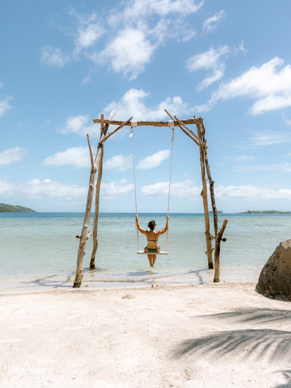 Woman swinging on a swing on beach at Pension Anahata on Taha’a , Tahiti
